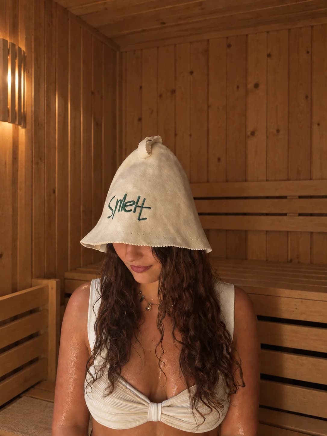 Woman wearing a Natural Cream Smelt sauna hat while seated in a wooden sauna